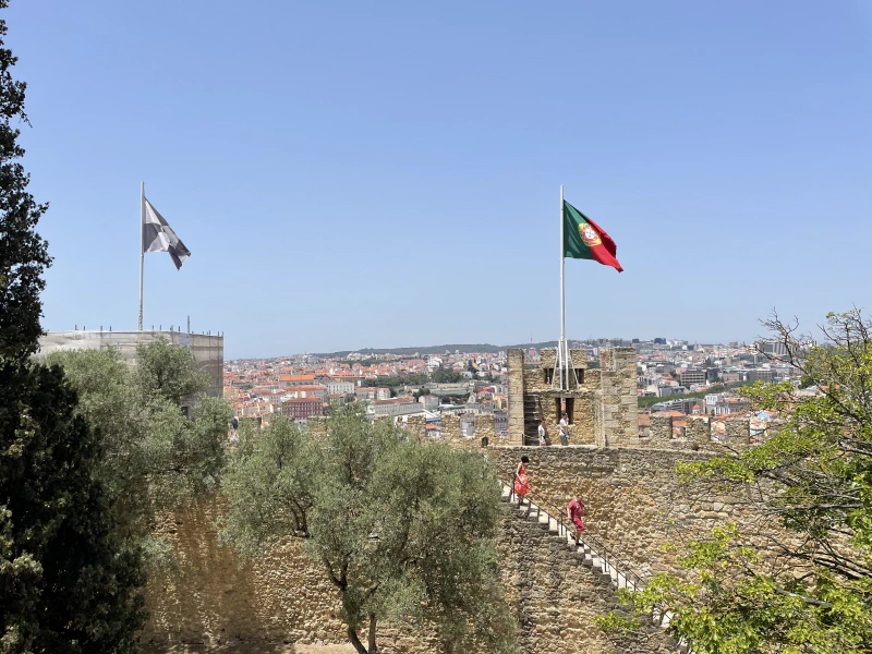 A view of the castle walls with the Portuguese flag flying atop. The city can be seen in the background